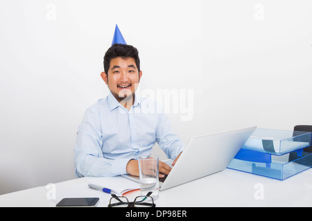 Portrait of happy businessman wearing party hat sitting at desk in office Stock Photo