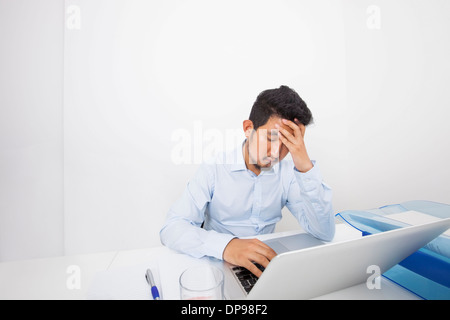 Stressed businessman with laptop sitting at desk in office Stock Photo