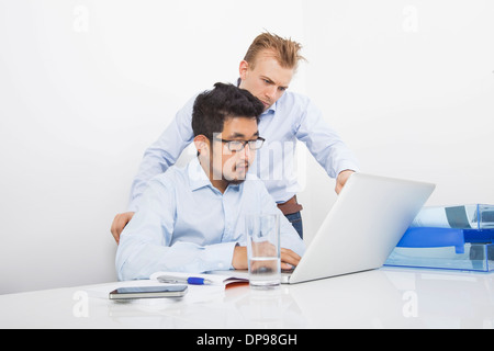 Businessmen using laptop together at desk in office Stock Photo