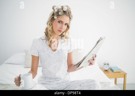 Peaceful cute blonde wearing hair curlers holding newspaper Stock Photo