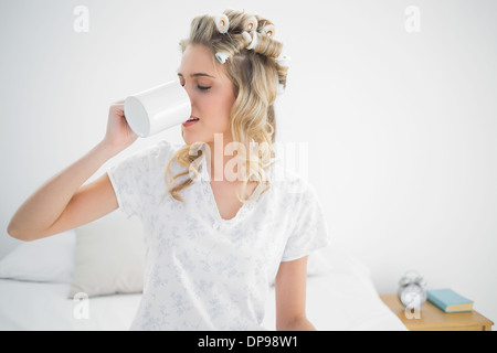 Cute blonde wearing hair curlers drinking coffee Stock Photo