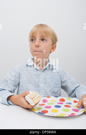 Cute boy with cake slice in plate on table looking away at home Stock Photo