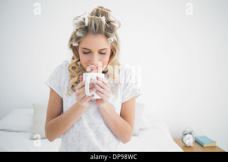 Peaceful cute blonde wearing hair curlers smelling coffee Stock Photo
