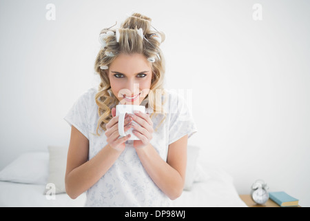 Smiling cute blonde wearing hair curlers smelling coffee Stock Photo