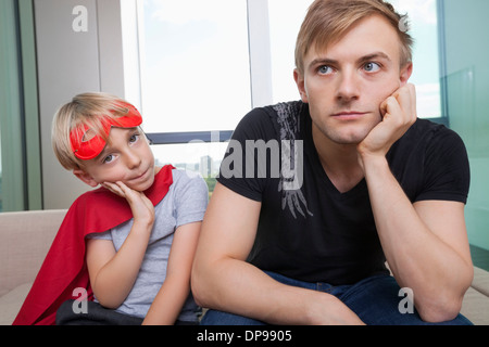Portrait of sad boy dressed in superhero costume sitting with father on sofa bed at home Stock Photo