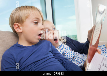 Shocked brother and sister reading storybook at home Stock Photo