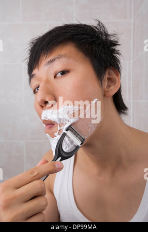 Portrait of mid adult Asian man shaving in bathroom Stock Photo