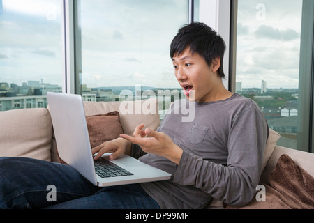 Shocked man using laptop on sofa at home Stock Photo