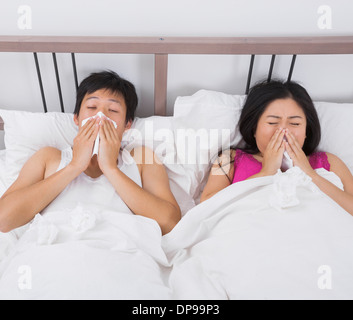 Young couple blowing noses in bed Stock Photo