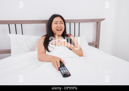 Happy woman watching TV in bed Stock Photo