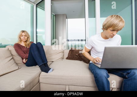 Sad woman beside man using laptop in living room at home Stock Photo