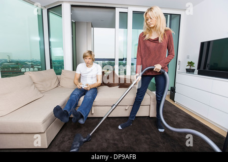 Woman vacuuming while man play video game in living room at home Stock Photo