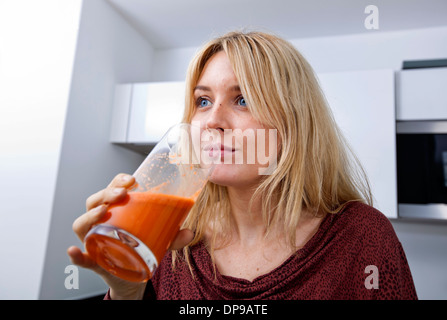 Young woman drinking carrot juice in kitchen Stock Photo