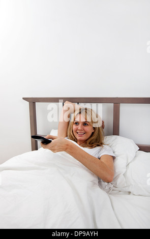 Happy young woman changing channels with remote control in bed Stock Photo