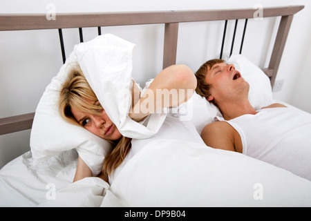 Frustrated woman covering ears with pillow while man snoring in bed Stock Photo