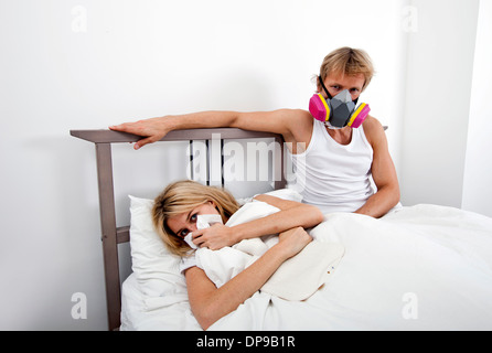 Portrait of man wearing gas mask while woman suffering from cold in bed Stock Photo