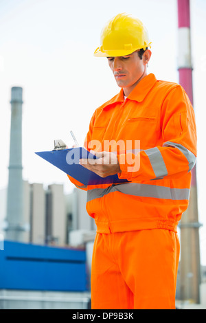 Male architect in protective workwear writing on clipboard at site Stock Photo