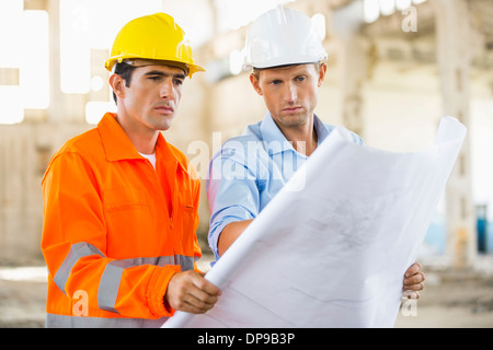 Male architects analyzing blueprint at construction site Stock Photo