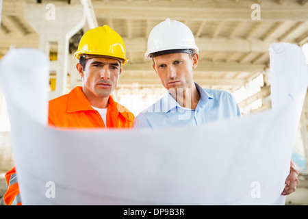 Male architects reviewing blueprint at construction site Stock Photo