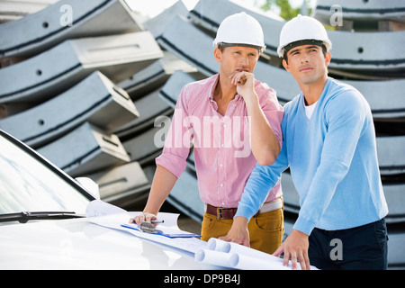 Architects with blueprints on car inspecting site Stock Photo