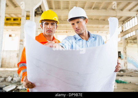 Male architects discussing over blueprint at construction site Stock Photo
