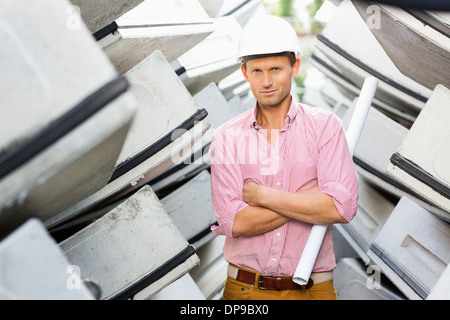 Portrait of male architect holding rolled up blueprint at construction site Stock Photo