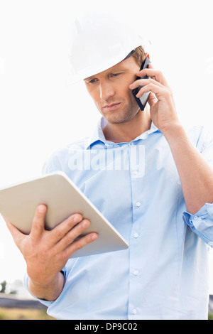 Male architect with digital tablet using cell phone at site Stock Photo