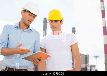 Male construction workers discussing over digital tablet at industry Stock Photo