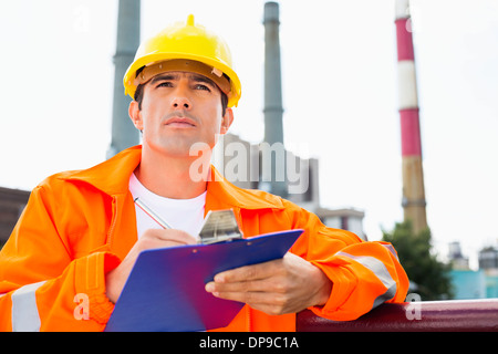 Male construction worker writing on clipboard at industry Stock Photo