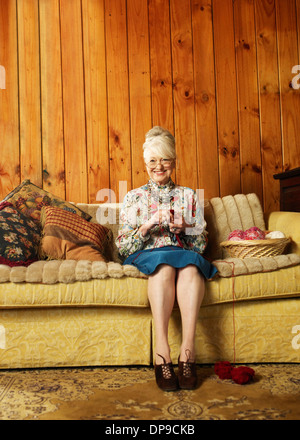Portrait of happy senior woman knitting on sofa at home Stock Photo