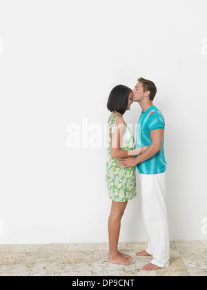 Loving young man kissing woman's forehead against wall Stock Photo