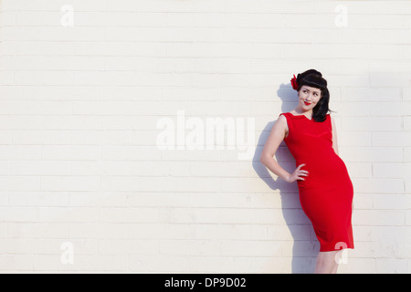 Young beautiful woman in red dress leaning on wall