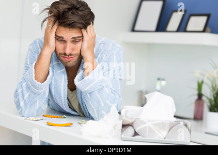 Young ill man suffering from headache at kitchen counter Stock Photo