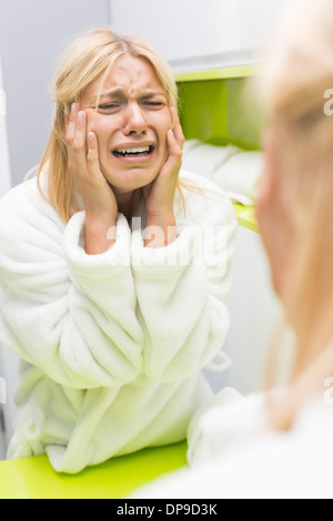 Young ill woman crying while looking at mirrior in bathroom Stock Photo