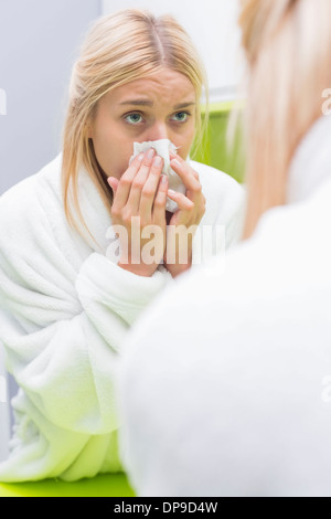 Young woman blowing nose in tissue paper while looking at mirror Stock Photo