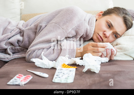 Sad woman with tissue and medicines lying on bed