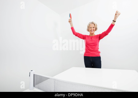 Portrait of senior female table tennis player with arms raised celebrating victory Stock Photo