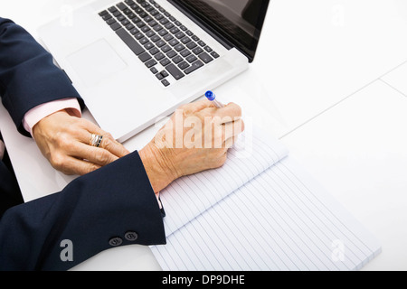 Cropped image of businesswoman with laptop writing in notebook on office desk Stock Photo