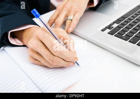 Cropped image of businesswoman with laptop writing in book on office desk Stock Photo