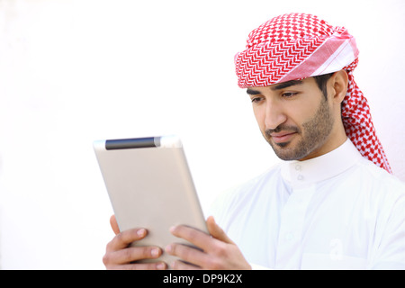 Arab man reading a tablet outdoor on a white wall Stock Photo