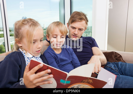 Father and children reading storybook on sofa at home Stock Photo