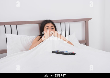 Frightened woman watching TV in bed Stock Photo