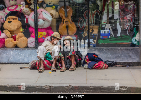 Indigenous man and woman begging while sitting on the sidewalk in front of a store window in Sucre, Bolivia. Stock Photo