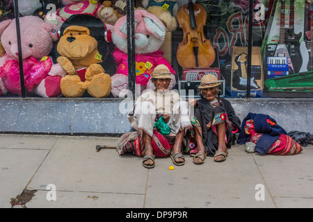 Indigenous man and woman begging while sitting on the sidewalk in front of a store window in Sucre, Bolivia. Stock Photo