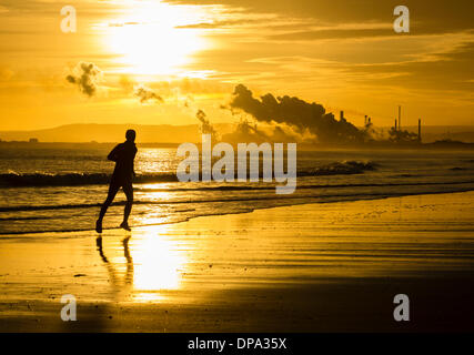 Man running on North Gare beach at sunrise.Redcar Steelworks in on the south side of the Tees estuary, Teesmouth in background. England. UK Stock Photo