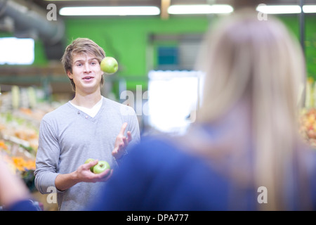 Young man juggling apples in indoor market Stock Photo