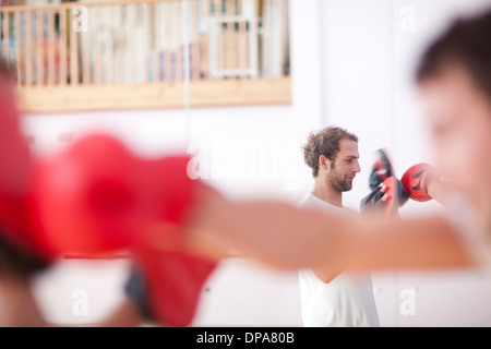 Young man and trainer boxing in gym Stock Photo