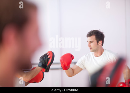 Young man and trainer boxing in sports hall Stock Photo