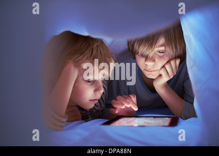 Brothers underneath duvet using digital tablet Stock Photo