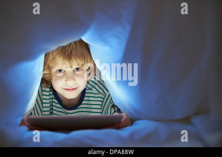 Boy underneath duvet using digital tablet Stock Photo
